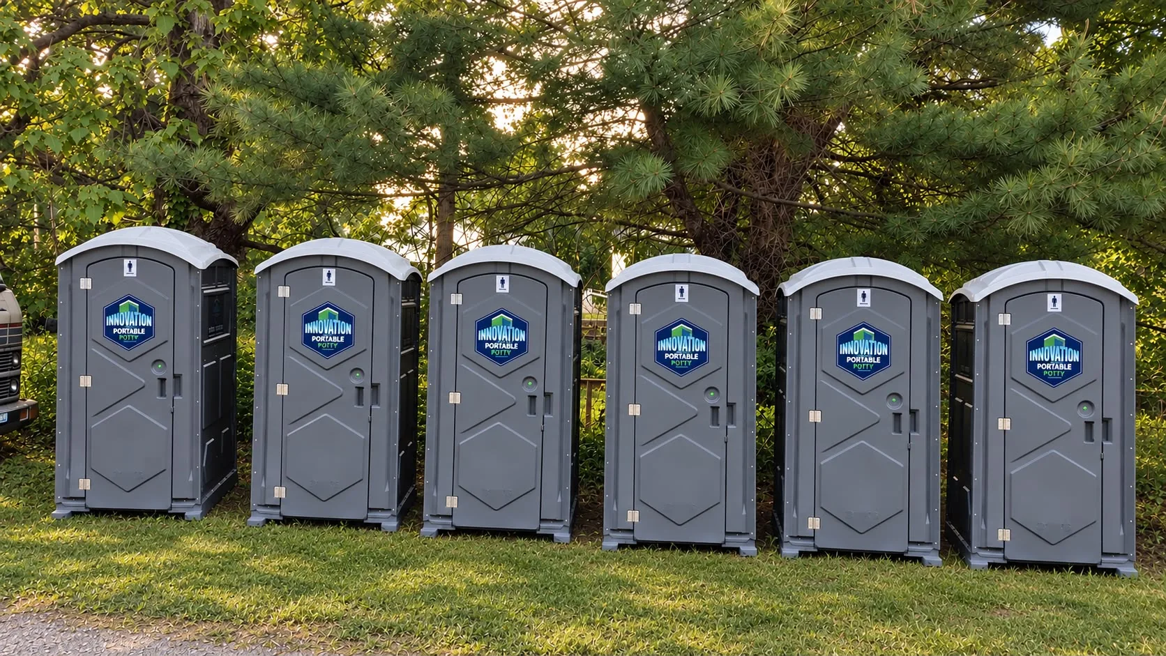 Six Innovation Portable Potty units lined up outdoors beneath trees